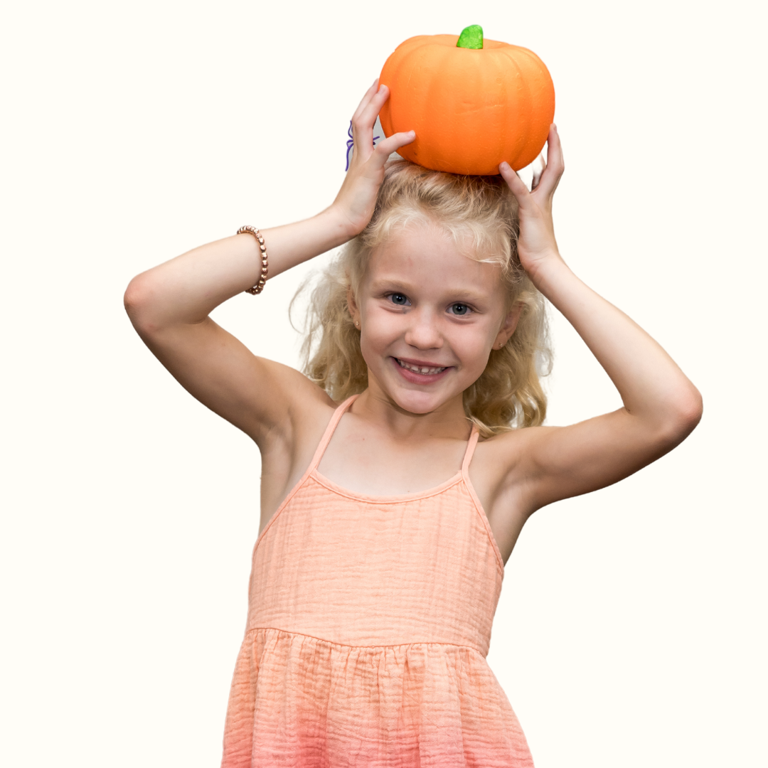 Elementary student holding a pumpkin on their head